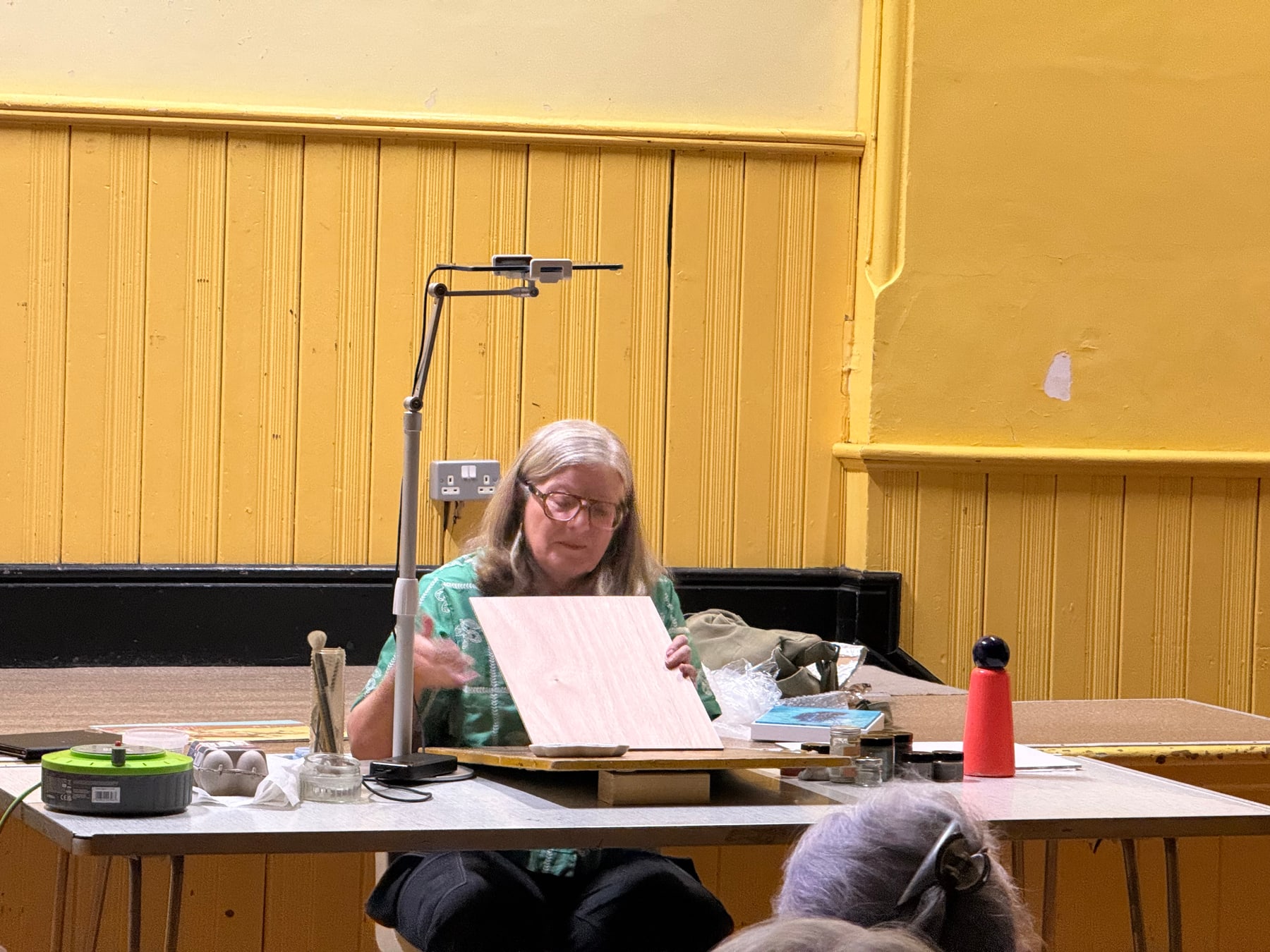 Jill Iliffe holds a pale prepared painting board at the front of the room.